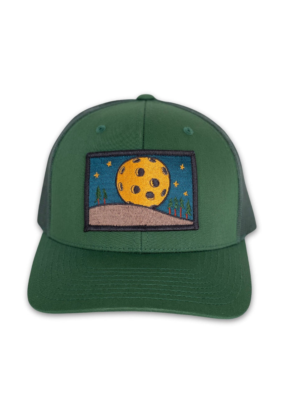 Trucker hat with a low profile. Front bill and panel is hunter green fabric. A yellow pickleball moon over a tan hill with green trees is embroidered on a patch in the center. The back panel is also green made of mesh with a snapback closure.