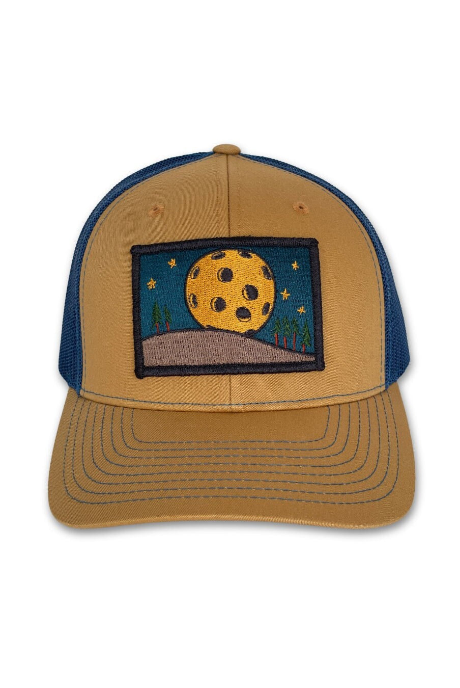 Trucker hat with a low profile. Front bill and panel is tan cotton fabric. A yellow pickleball moon over a tan hill with green trees is embroidered on a patch in the center. The back panel is blue made of mesh with a snapback closure.