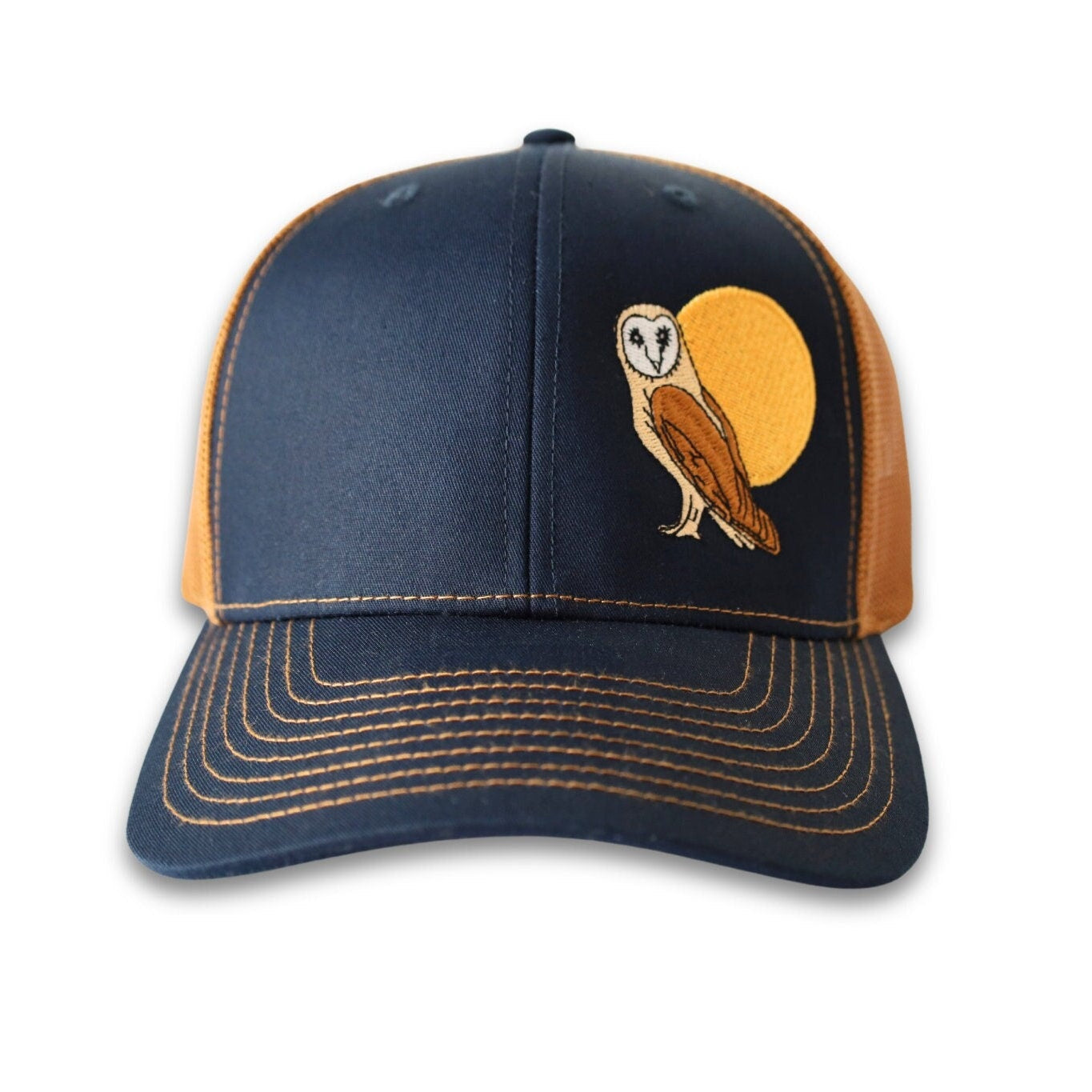 Trucker hat with a low profile. Front bill and panel is navy soft cotton fabric. A brown and tan owl and big yellow moon is embroidered on the side front. The back panel is caramel colored made of mesh with a snapback closure.